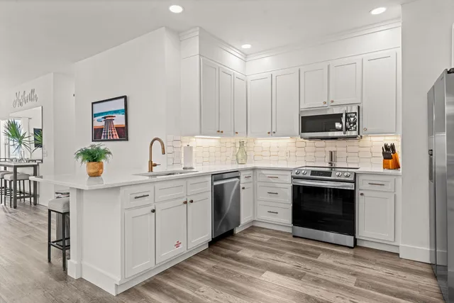 a kitchen with stainless steel appliances granite countertop a stove top oven a sink dishwasher and a refrigerator with wooden floor