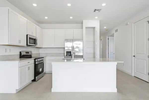 a large kitchen with stainless steel appliances granite countertop a stove a sink a refrigerator and white cabinets