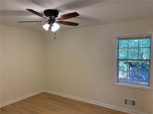 an empty room with wooden floor fan and windows