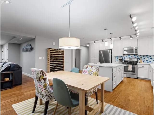 a kitchen with stainless steel appliances kitchen island granite countertop a dining table chairs and a refrigerator