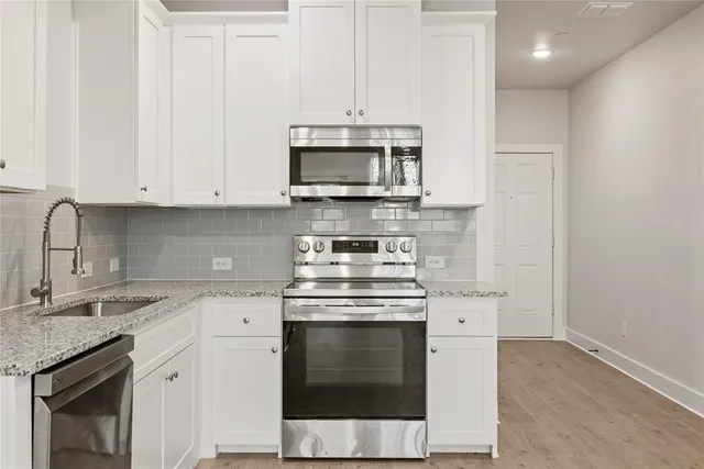 a kitchen with stainless steel appliances granite countertop a stove and a white cabinet