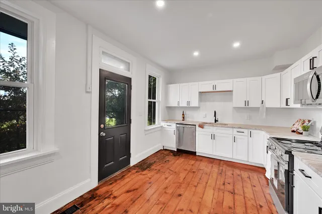 a kitchen with stainless steel appliances kitchen island granite countertop a refrigerator oven a sink dishwasher and white cabinets with wooden floor