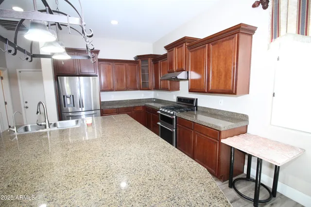 a kitchen with stainless steel appliances granite countertop a stove a sink and a refrigerator with wooden cabinets