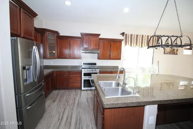 a kitchen with stainless steel appliances granite countertop a refrigerator a stove and a sink with wooden floors