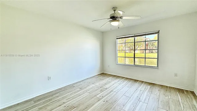 an empty room with wooden floor fan and windows