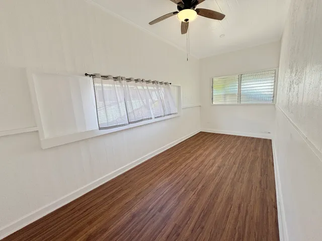 an empty room with wooden floor chandelier fan and windows