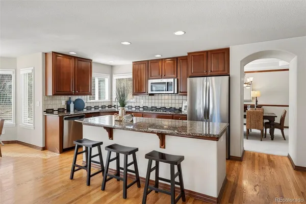 a kitchen with stainless steel appliances granite countertop a refrigerator a stove a sink and white cabinets with wooden floor