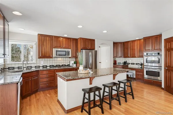 a kitchen with stainless steel appliances granite countertop a stove top oven a sink dishwasher a dining table and chairs with wooden floor