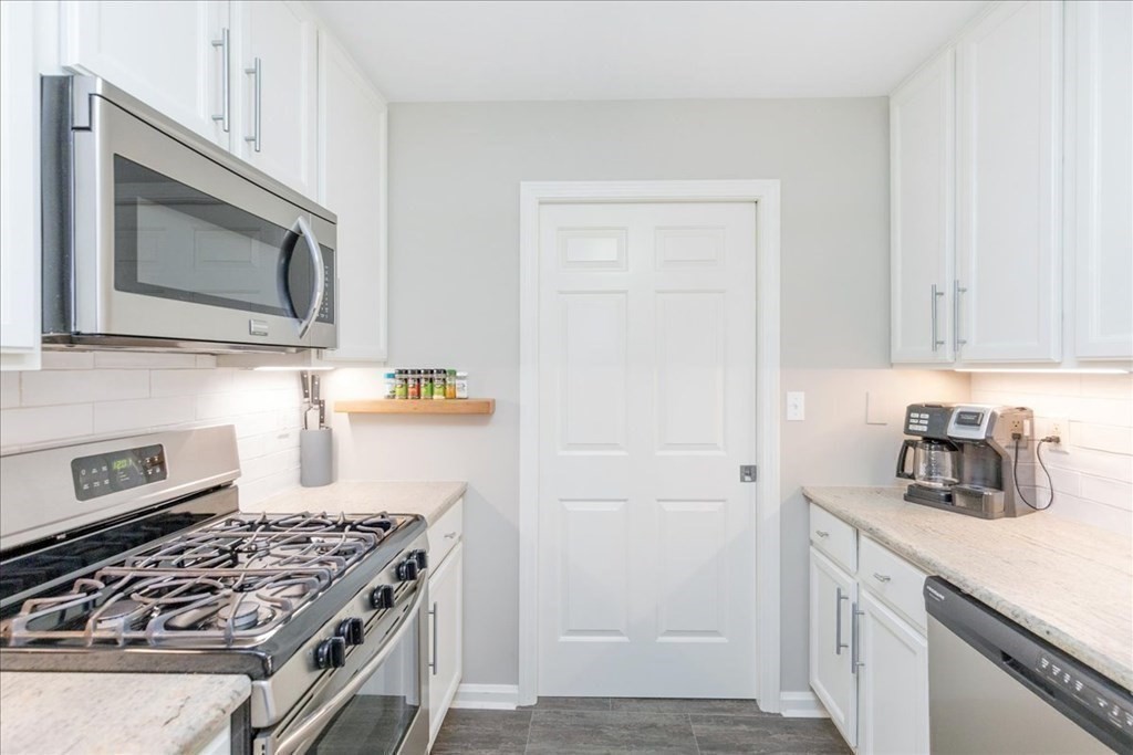 38 Village Road, Unit 312 Middleton, MA 01949 - Photo 9 of 42 a kitchen with stainless steel appliances granite countertop white cabinets and black stove top oven with wooden floor