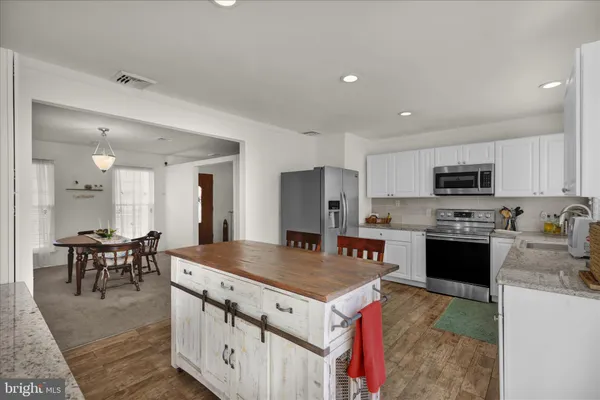 a kitchen with stainless steel appliances granite countertop a stove top oven a sink dishwasher a dining table and chairs with wooden floor