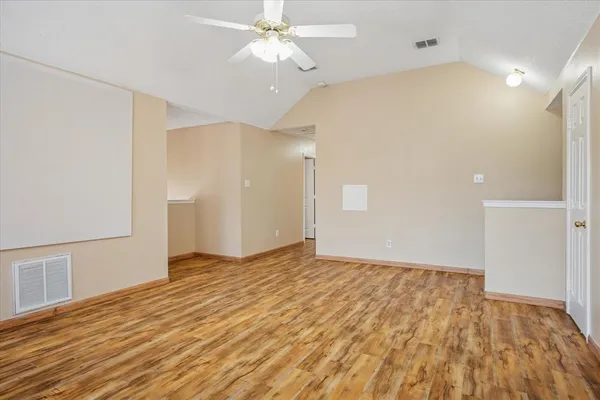 a view of an empty room with wooden floor and a ceiling fan