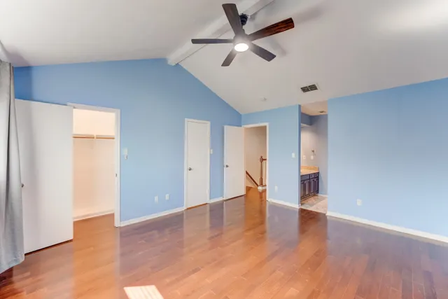 a view of an empty room with wooden floor and a ceiling fan