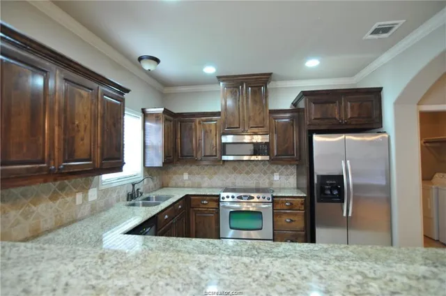 a kitchen with stainless steel appliances granite countertop a sink a stove a refrigerator a washer and dryer