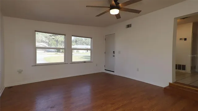 an empty room with wooden floor fan and windows