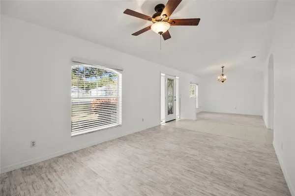 an empty room with chandelier fan and windows