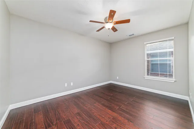 an empty room with wooden floor fan and windows