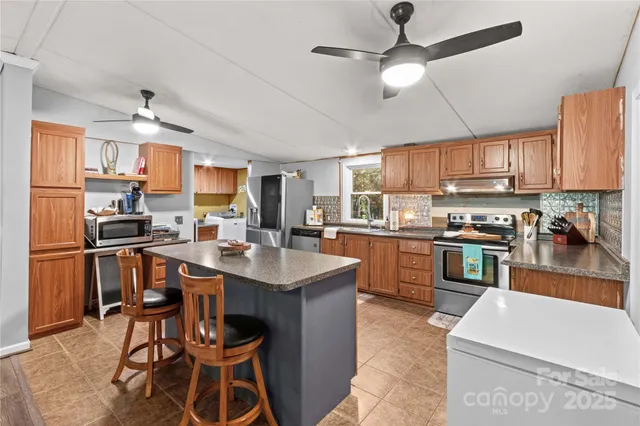 a kitchen with stainless steel appliances kitchen island granite countertop a sink a stove a refrigerator cabinets and chairs