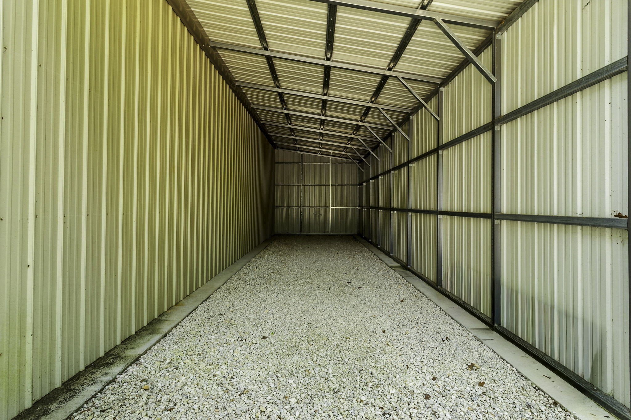 21 Red Oak Circle Point Blank, TX 77364 - Photo 29 of 32 This photo shows a spacious, metal-sided storage shed with a gravel floor, ideal for storing vehicles or equipment.