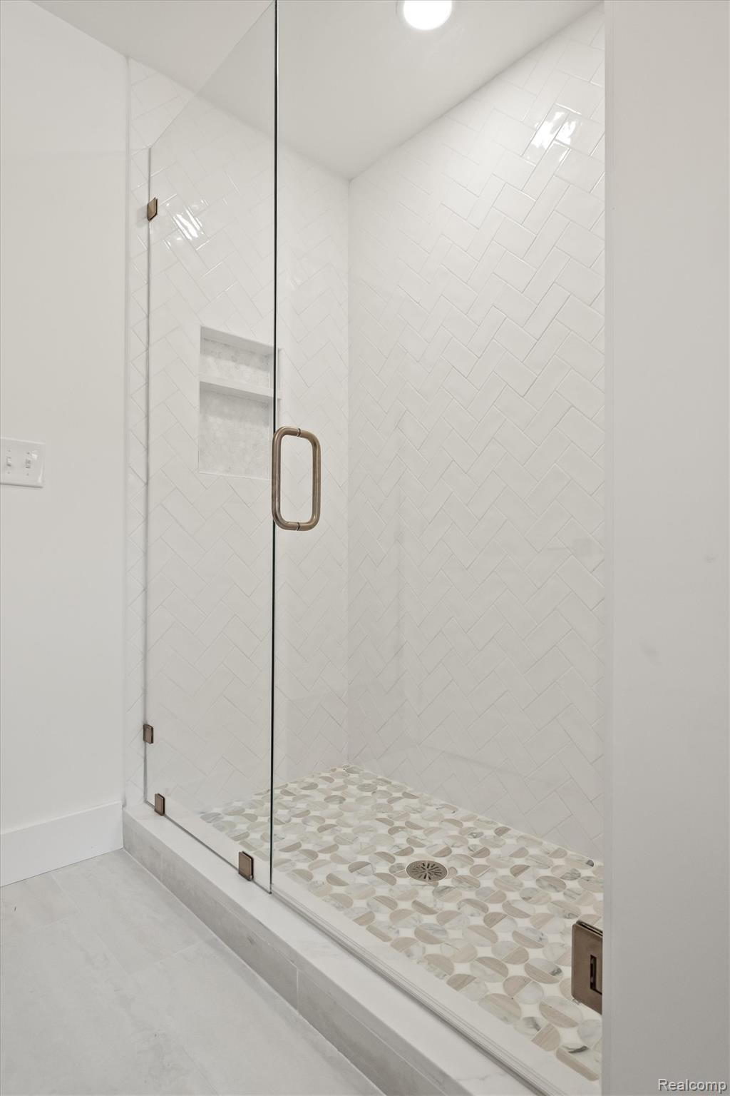 347 Highland Avenue Rochester, MI 48307 - Photo 24 of 59 Glass-enclosed shower featuring a white chevron-patterned tile surround, a pebble-style mosaic floor, and a built-in shower niche