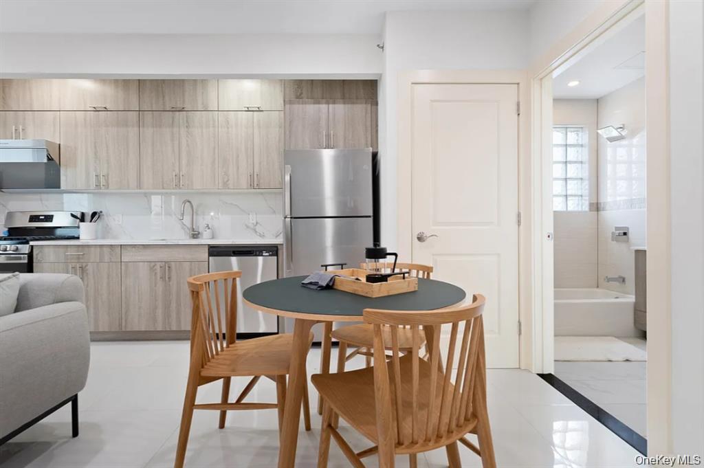 124-28 Queens Boulevard, Unit 12B Queens, NY 11415 - Photo 4 of 9 Kitchen featuring appliances with stainless steel finishes, modern cabinets, light brown cabinets, exhaust hood, and backsplash
