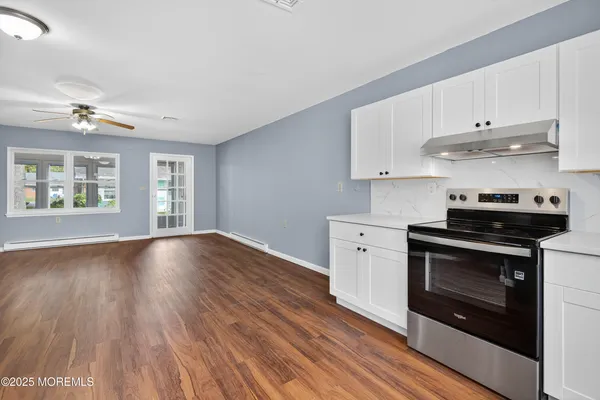 a kitchen with stainless steel appliances granite countertop a stove a sink and white cabinets with wooden floors