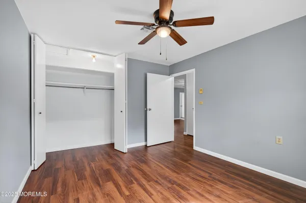 an empty room with wooden floor ceiling fan and windows