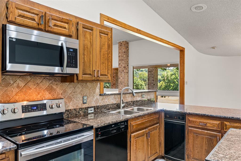 7508 Ravenswood Road Granbury, TX 76049 - Photo 18 of 40 a kitchen with stainless steel appliances granite countertop a stove a sink and a microwave
