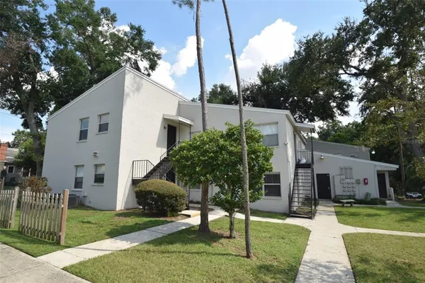 a view of a white house next to a yard with big trees