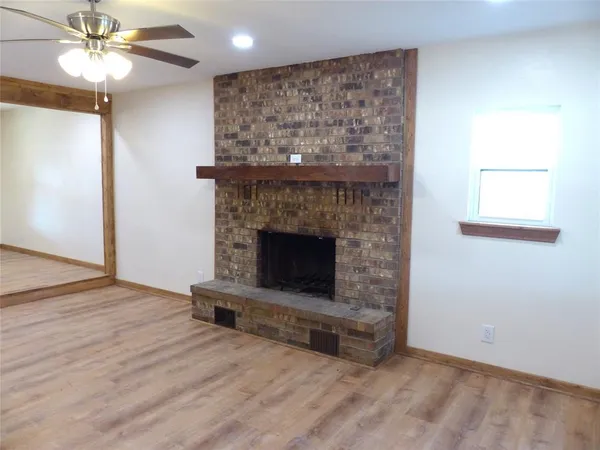 an empty room with wooden floor a ceiling fan a fireplace and windows