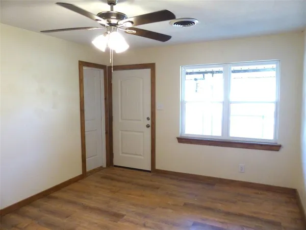 an empty room with wooden floor chandelier fan and windows