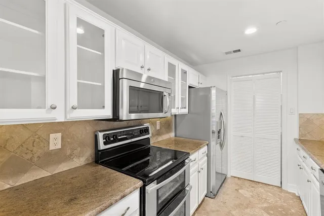 a kitchen with granite countertop a stove and a refrigerator with white cabinets