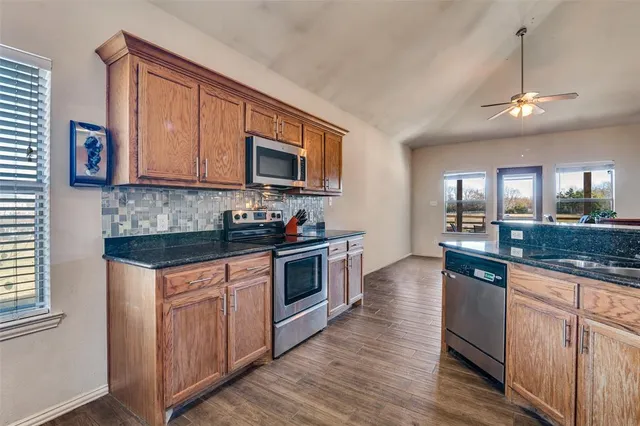 a kitchen with granite countertop a stove top oven a sink dishwasher and white cabinets with wooden floor