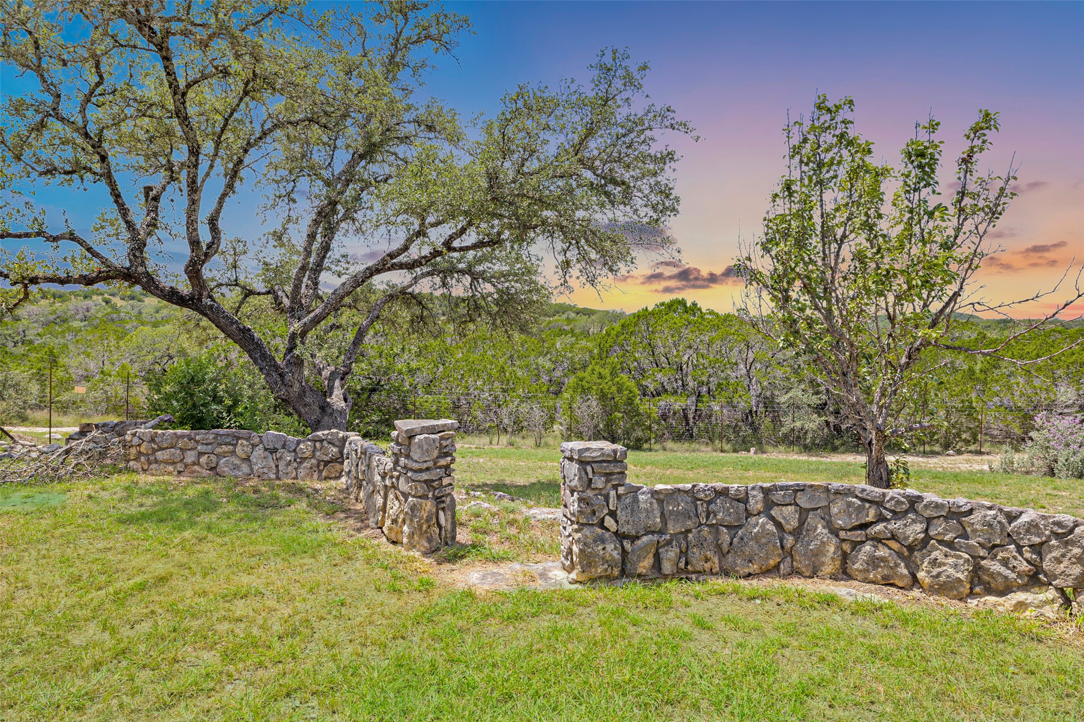 11151 Highway 71 Spicewood, TX 78669 - Photo 17 of 38 Backyard of the estate highlighted by a stone wall, expansive greenbelt views, and majestic oak trees.