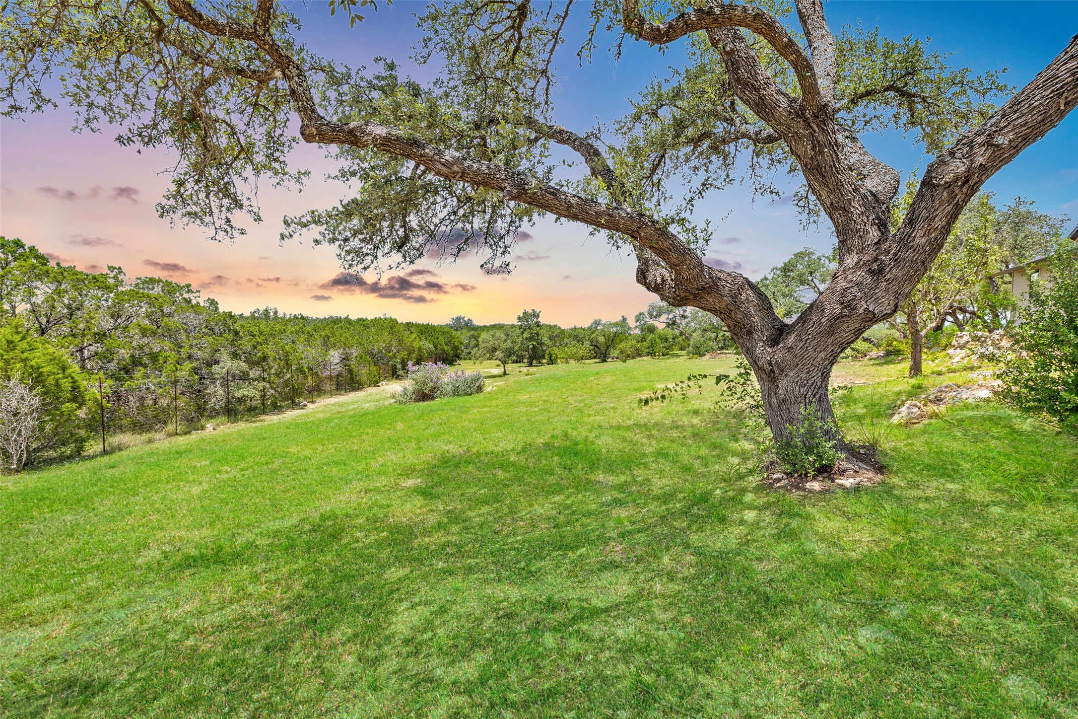 11151 Highway 71 Spicewood, TX 78669 - Photo 29 of 38 Backyard at dusk highlighting a serene lawn and sweeping countryside views with beautiful oak trees.