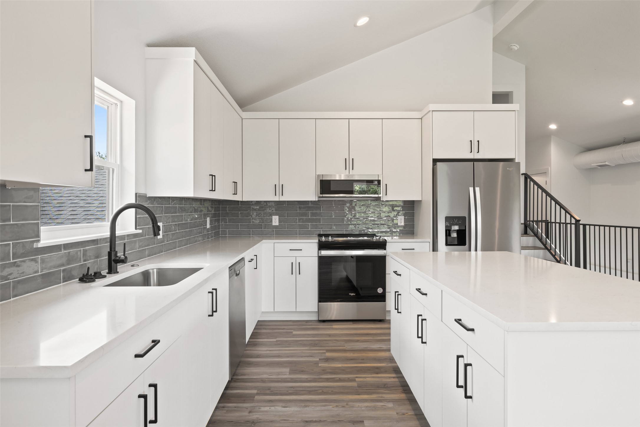 11151 Highway 71 Spicewood, TX 78669 - Photo 32 of 38 Third Residence - Kitchen showcasing stainless steel appliances, a center island, vaulted ceiling, white cabinetry, and wood-style LVP flooring; refrigerator included.