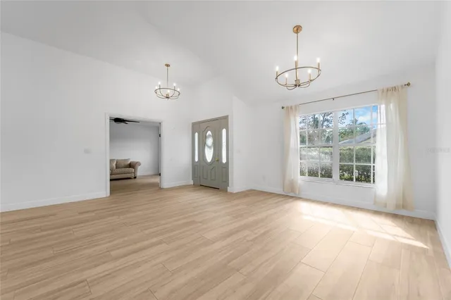 an empty room with wooden floor chandelier and windows