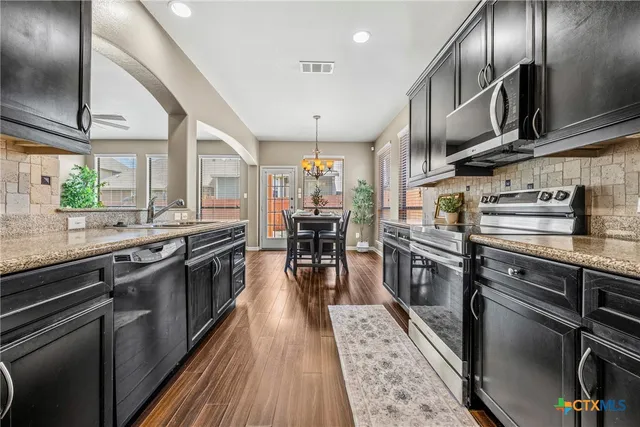 a kitchen with stainless steel appliances granite countertop a stove top oven a sink dishwasher a refrigerator and cabinets with wooden floor