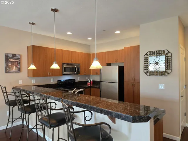 a kitchen with stainless steel appliances granite countertop a stove a refrigerator a sink a dining table and chairs