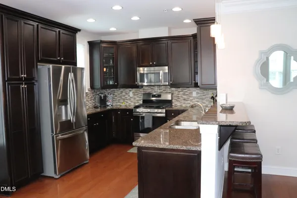 a kitchen with stainless steel appliances kitchen island granite countertop a refrigerator a stove a sink a dining table and chairs with wooden floor