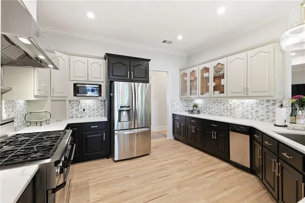 a kitchen with stainless steel appliances granite countertop a refrigerator a sink dishwasher a stove top oven a refrigerator with white cabinets and wooden floor