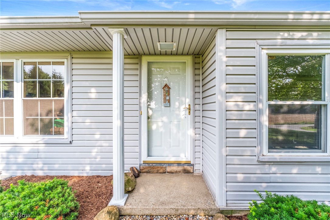 8360 Roller Road Salem, OH 44460 - Photo 3 of 45 Entryway featuring a white paneled door with a brass handle, light gray horizontal siding, a fluted column, a concrete stoop, and foundation plantings