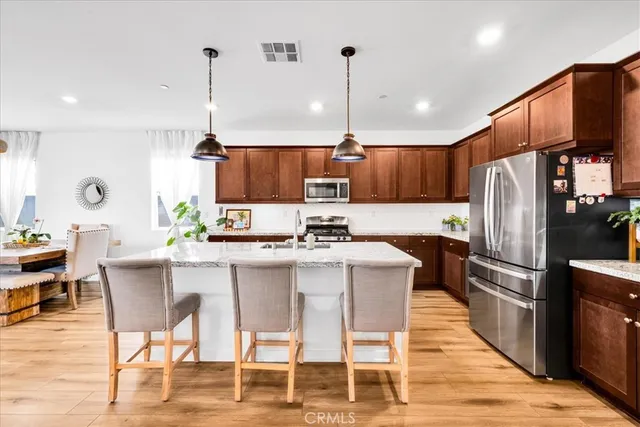 a kitchen with stainless steel appliances kitchen island granite countertop a refrigerator a stove a sink a center island and chairs with wooden floor