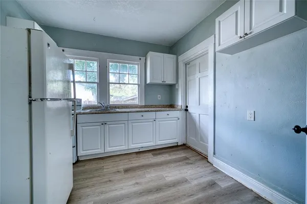 a kitchen with granite countertop a refrigerator and white cabinets