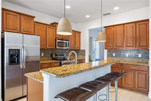 a kitchen with stainless steel appliances granite countertop a sink a stove a refrigerator cabinets and chairs