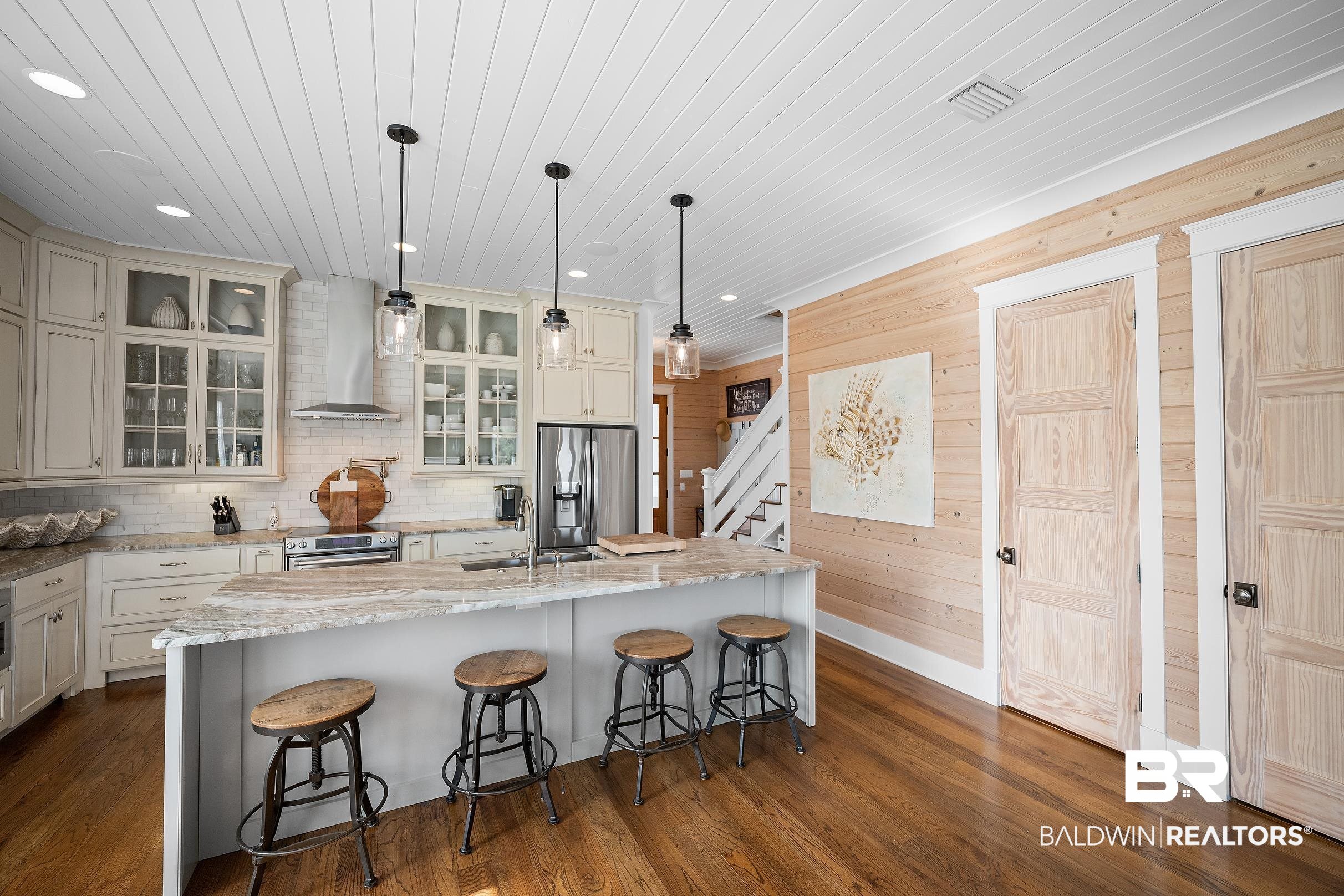 33186 Marlin Key Drive Orange Beach, AL 36561 - Photo 42 of 87 Kitchen featuring wood walls, decorative light fixtures, glass insert cabinets, light stone counters, and a kitchen bar