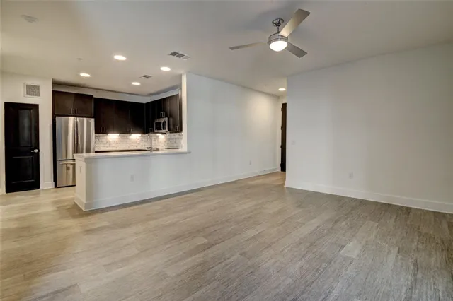 an empty room with wooden floor kitchen view and a window