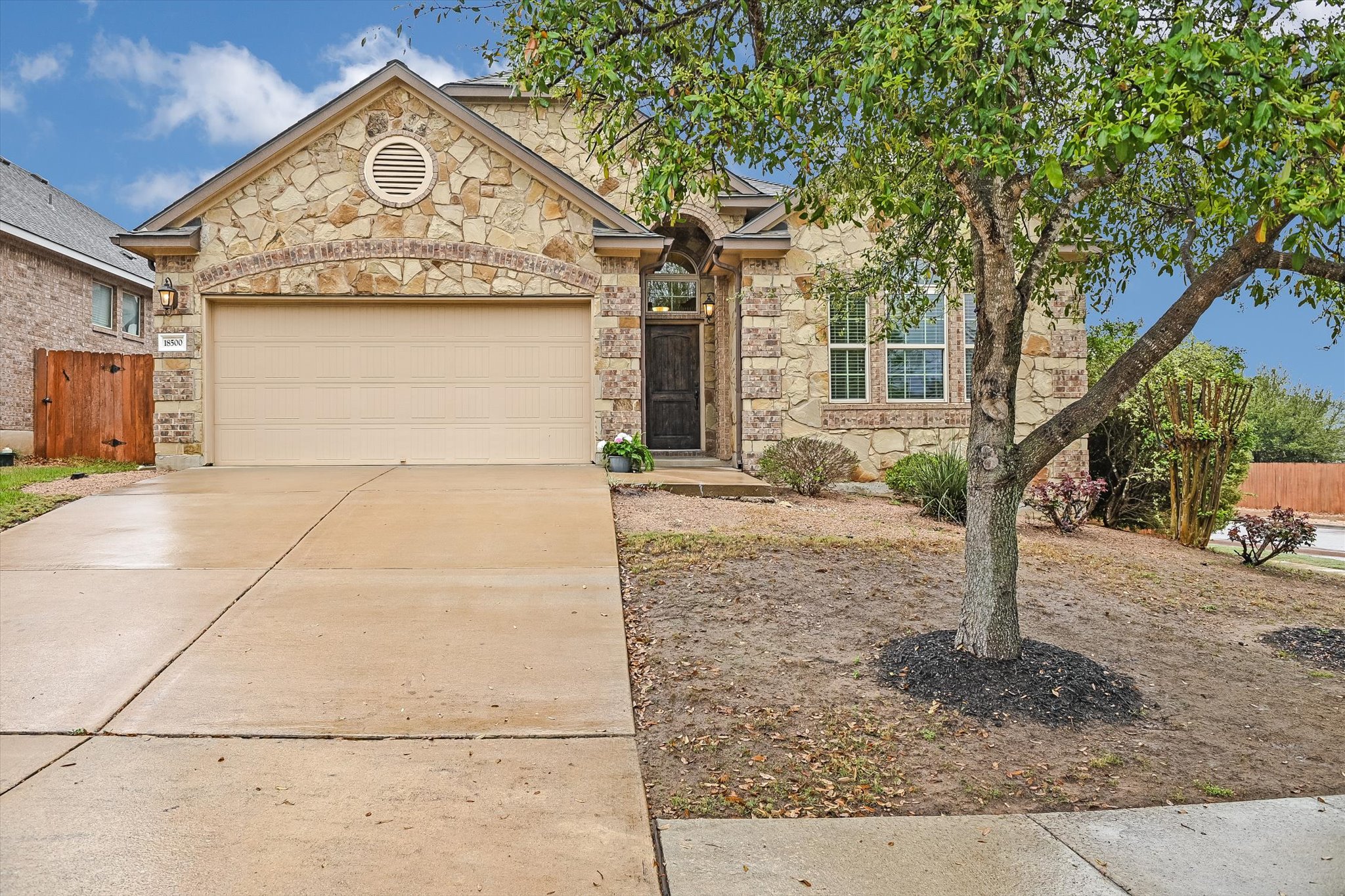 18500 Rio Chama Lane Austin, TX 78738 - Photo 1 of 28 Property exterior featuring a stone facade, an attached garage, a paved driveway, and a front yard with a mature tree