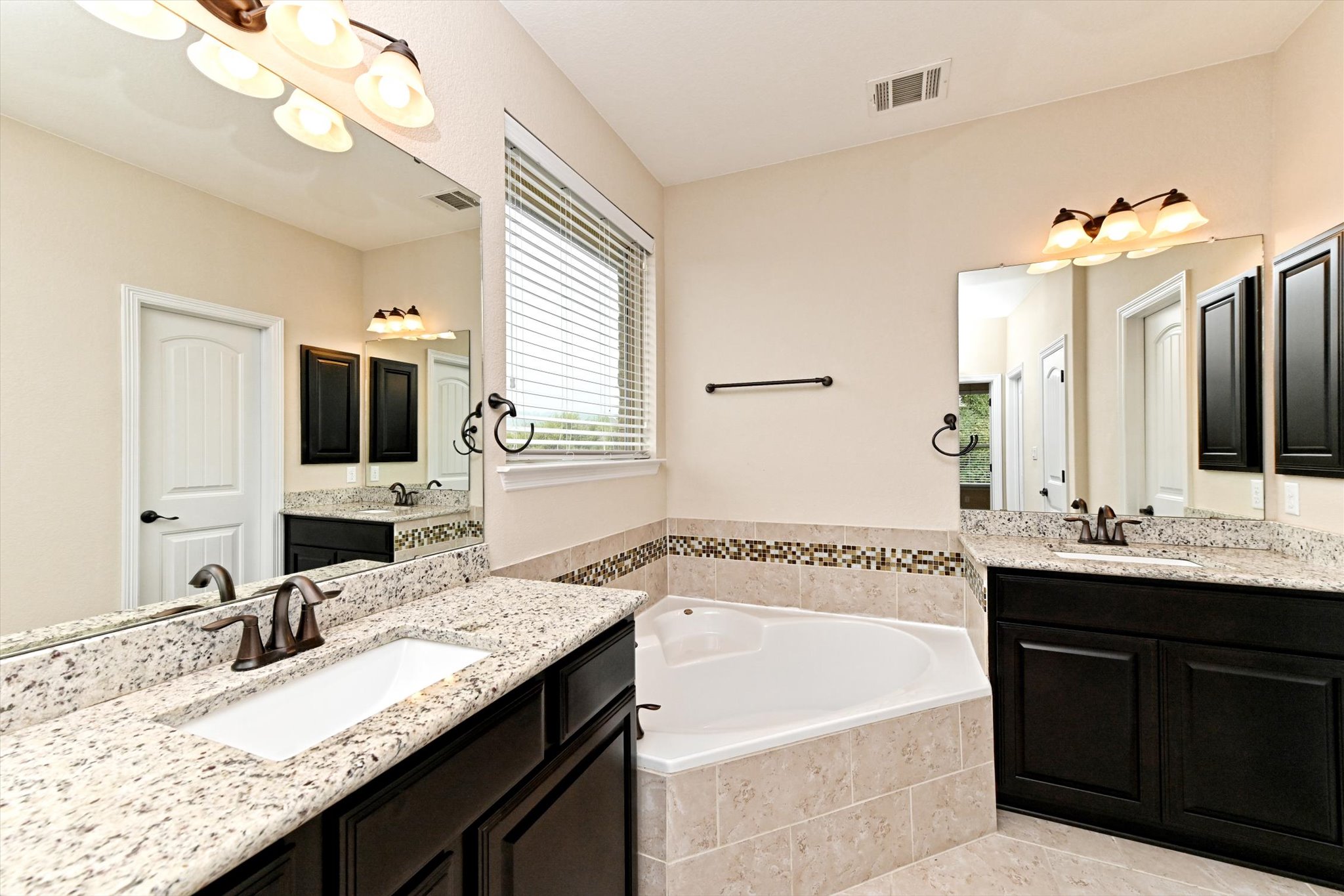 18500 Rio Chama Lane Austin, TX 78738 - Photo 20 of 28 Bathroom featuring dual vanities with granite countertops, a built-in corner bathtub, and a window with blinds