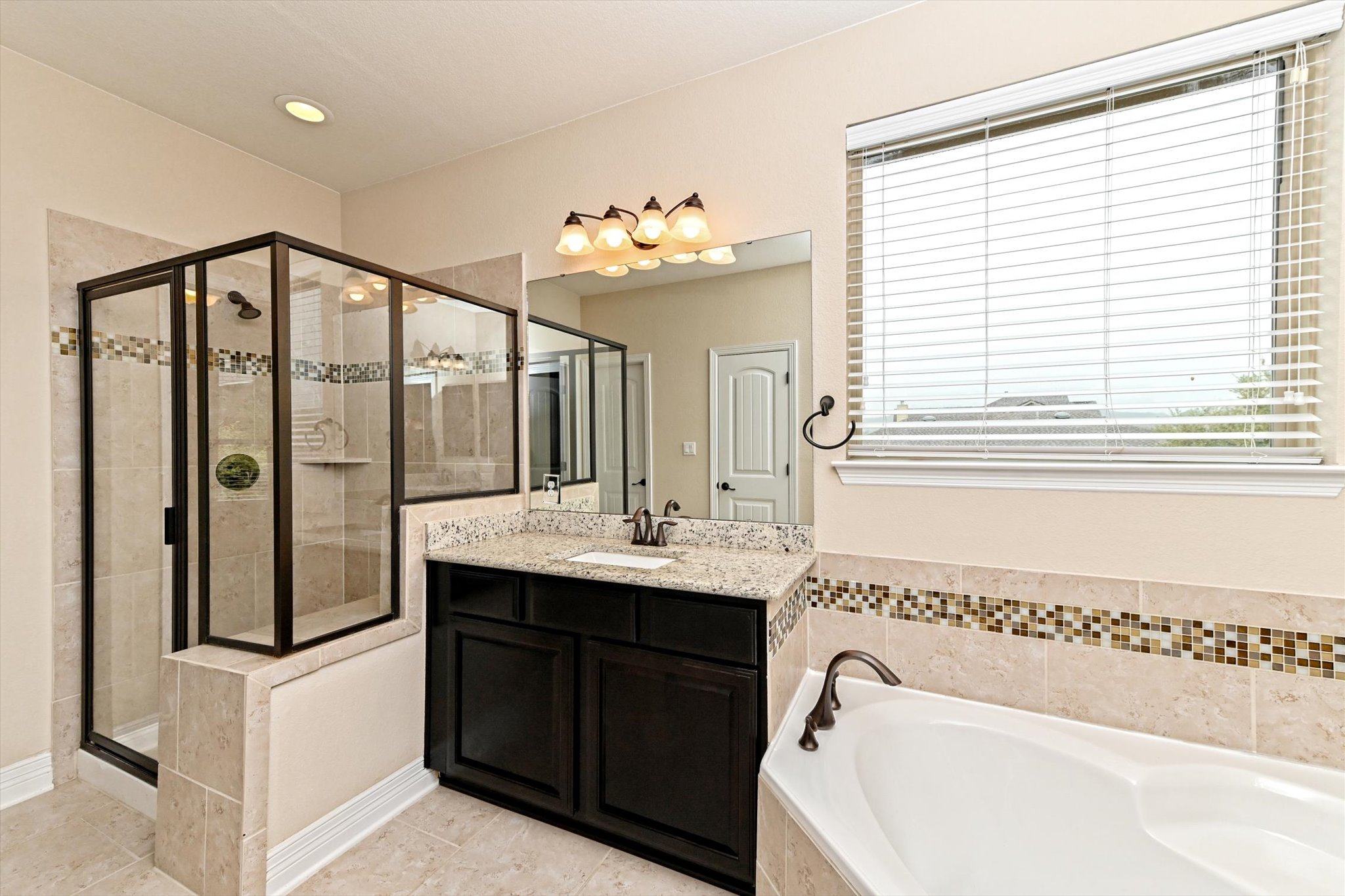 18500 Rio Chama Lane Austin, TX 78738 - Photo 21 of 28 Well-appointed bathroom featuring a glass-enclosed shower, a corner bathtub, and a vanity with a granite countertop and dark wood cabinetry