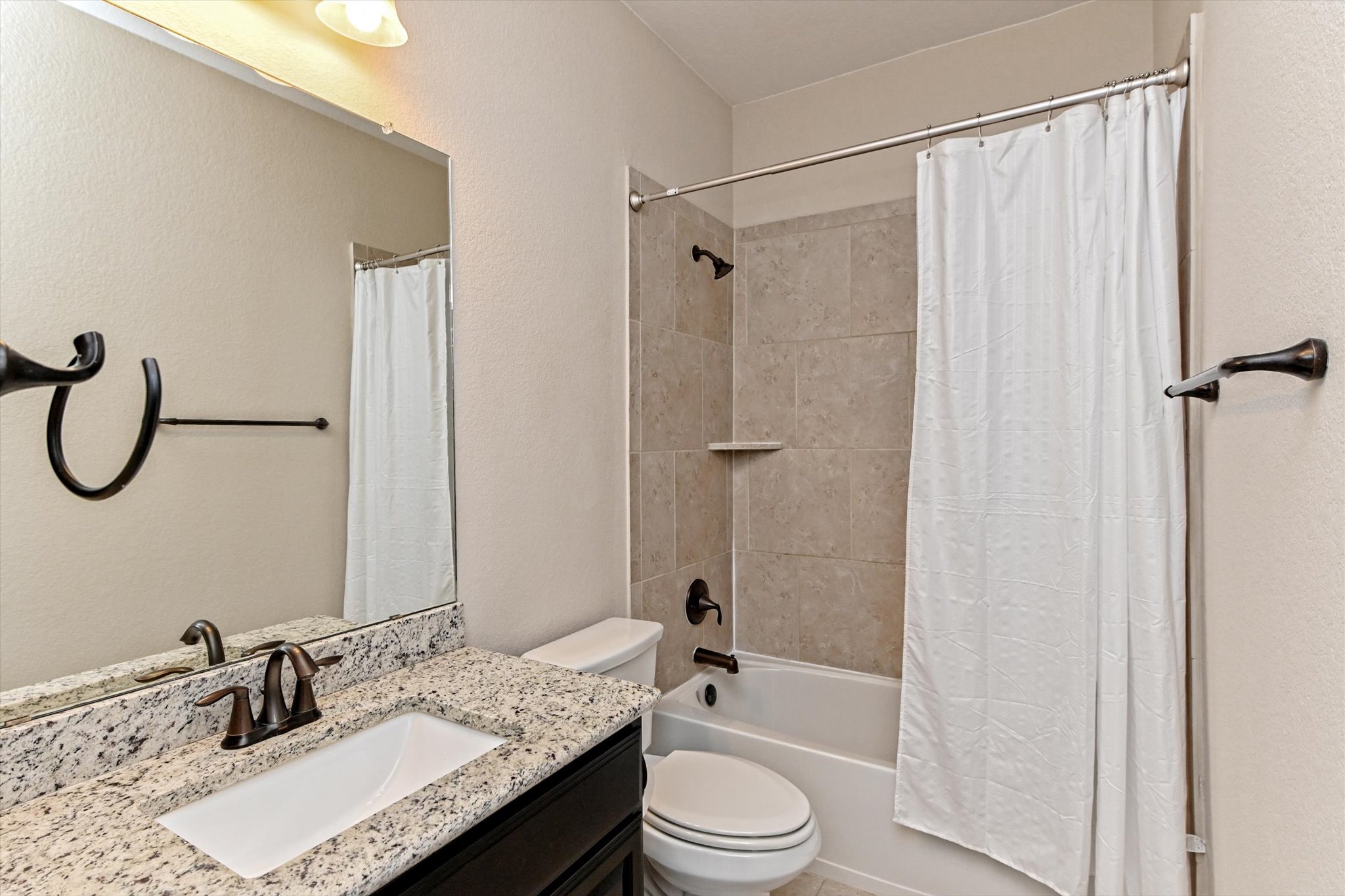 18500 Rio Chama Lane Austin, TX 78738 - Photo 25 of 28 Bathroom featuring a vanity with a granite countertop and an undermount sink, a toilet, and a combination shower and bathtub with a tiled surround